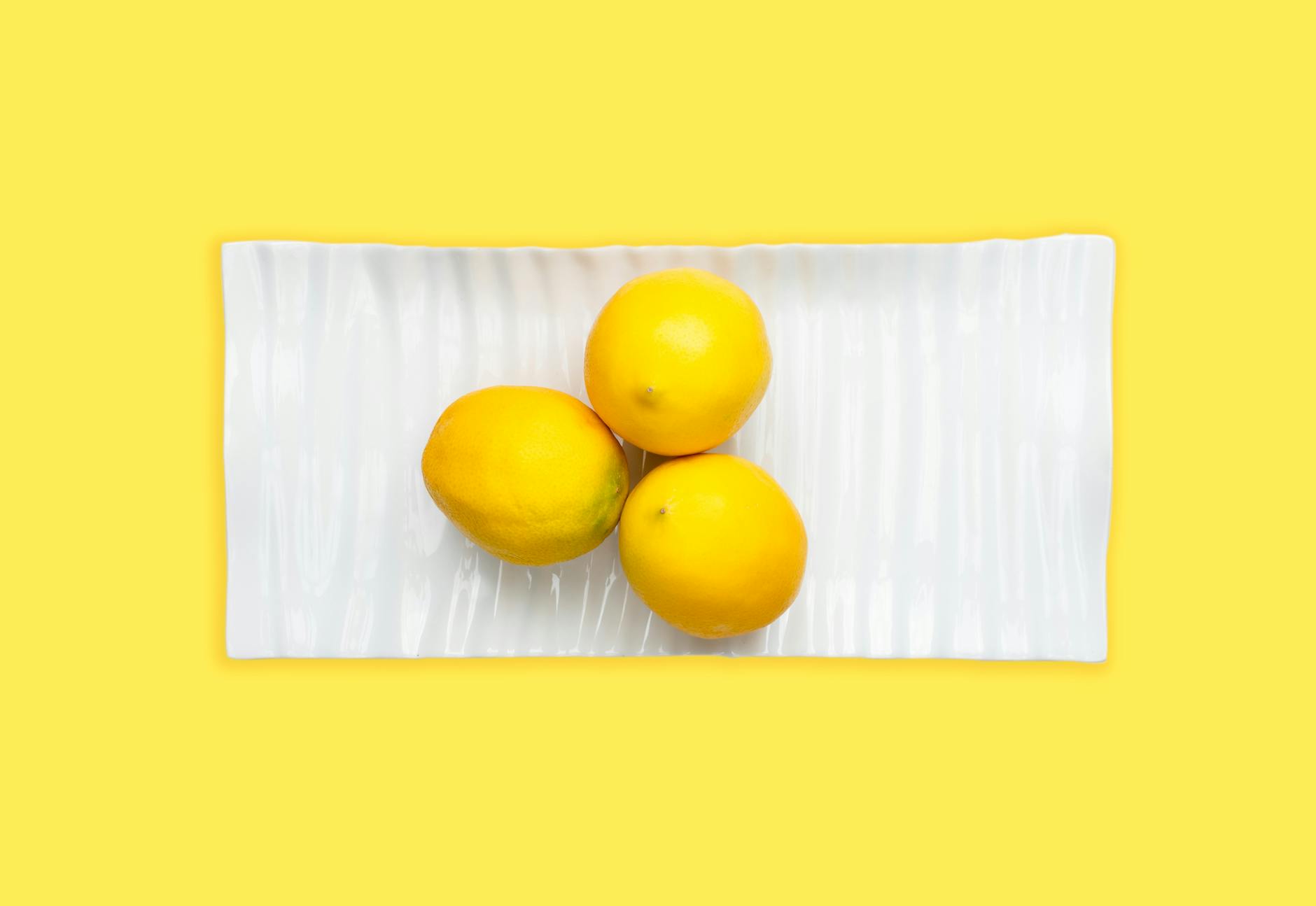 A blue clitoral vibrator surrounded by flowers and citrus slices on a bright yellow surface