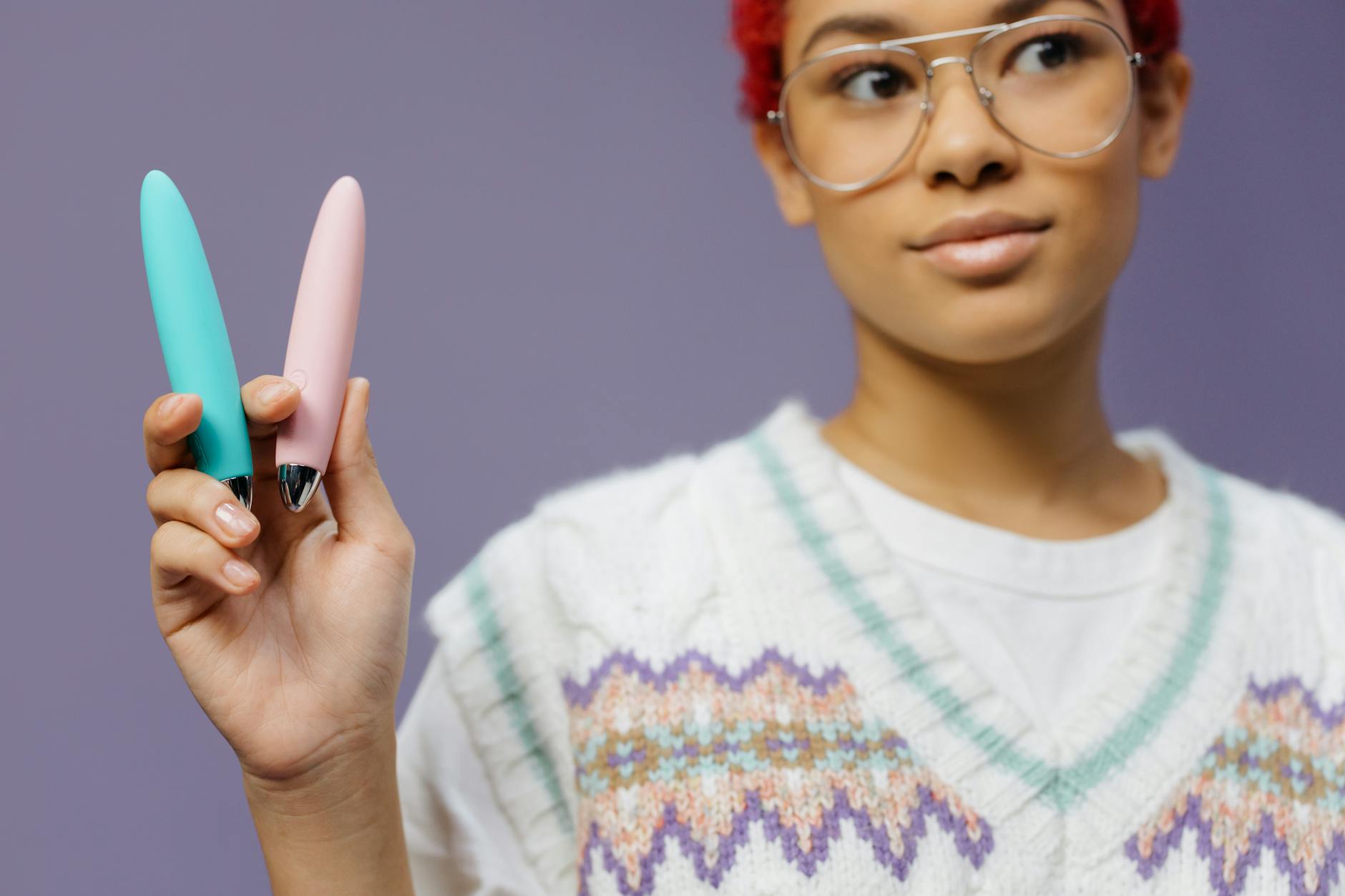 A woman holds two colorful personal massagers against a purple background